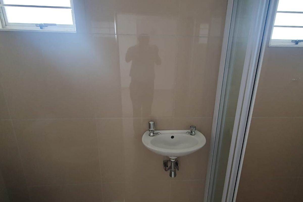 A compact bathroom featuring tiled walls, a wall-mounted basin, a toilet, and a shower enclosure with two small windows for natural light.
