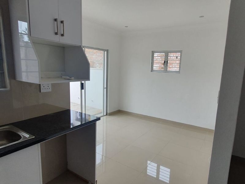 An open-plan kitchen and living area featuring modern cabinetry, granite countertops, tiled flooring, and direct access to an outdoor space via a sliding door.
