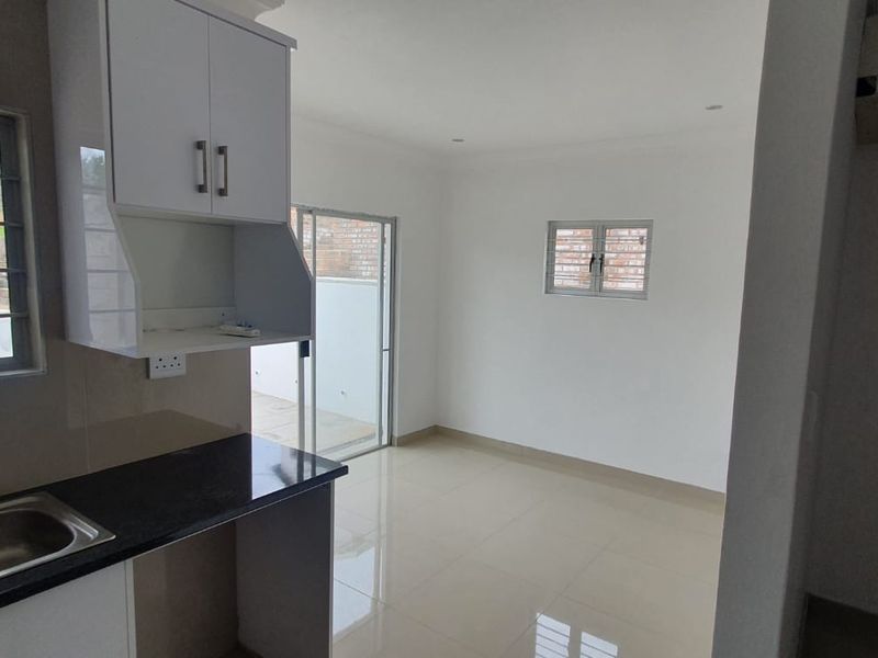 An open-plan kitchen and living area featuring modern white cabinetry, granite countertops, tiled floors, and direct access to an outdoor space via sliding doors.