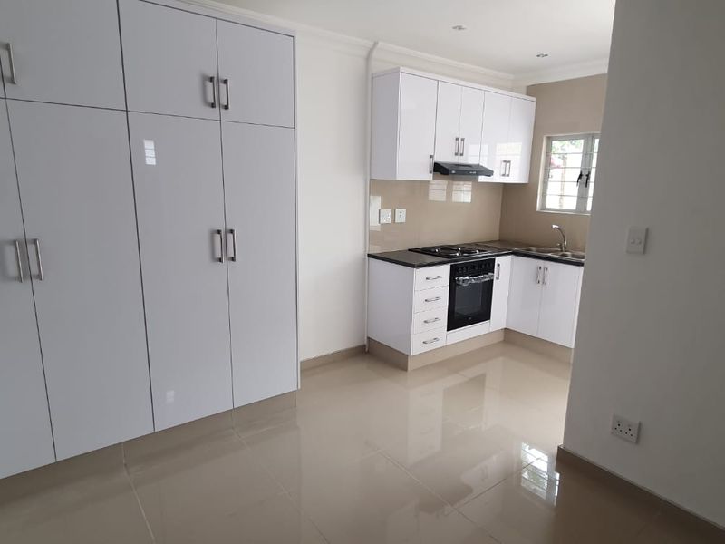 Modern kitchen featuring white high-gloss cabinetry, built-in oven and hob, stainless steel sink, and neutral tiled flooring in an open-plan layout.