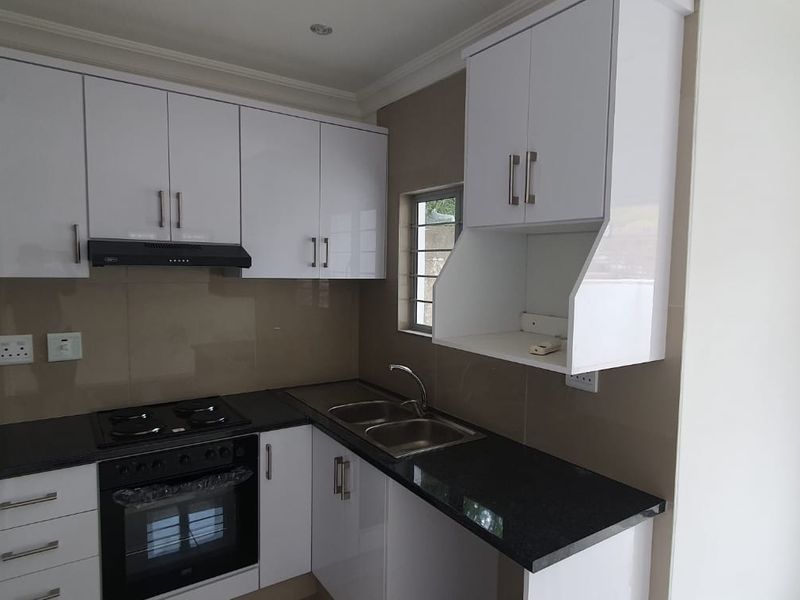 Modern kitchen featuring white cabinetry, black granite countertops, built-in oven, gas hob, extractor fan, and a stainless steel sink with tiled splashback.