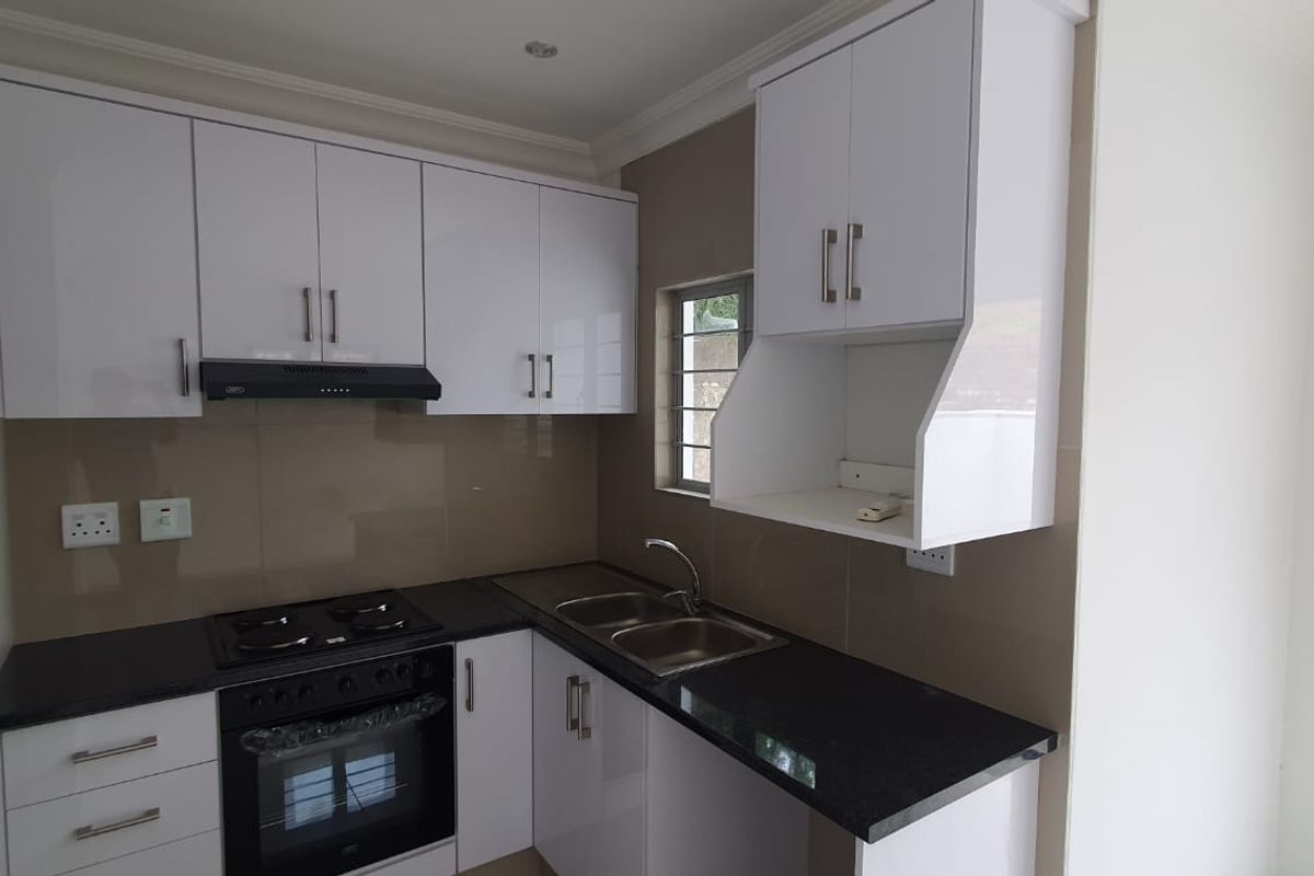 Modern kitchen featuring white high-gloss cabinetry, black granite countertops, a built-in oven, gas hob, and a sleek glass splashback.