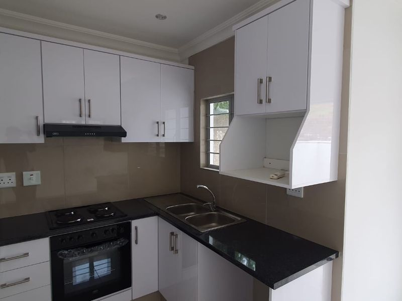 Modern kitchen featuring white high-gloss cabinetry, black granite countertops, a built-in oven, gas hob, and a sleek glass splashback.