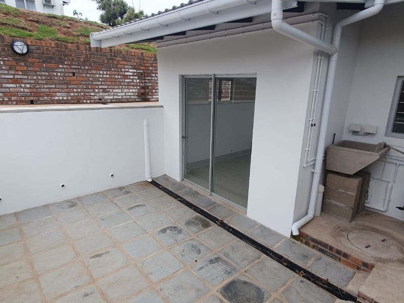 A paved outdoor patio area featuring a sliding door entrance, a concrete wash basin, and an external electric water heater unit.