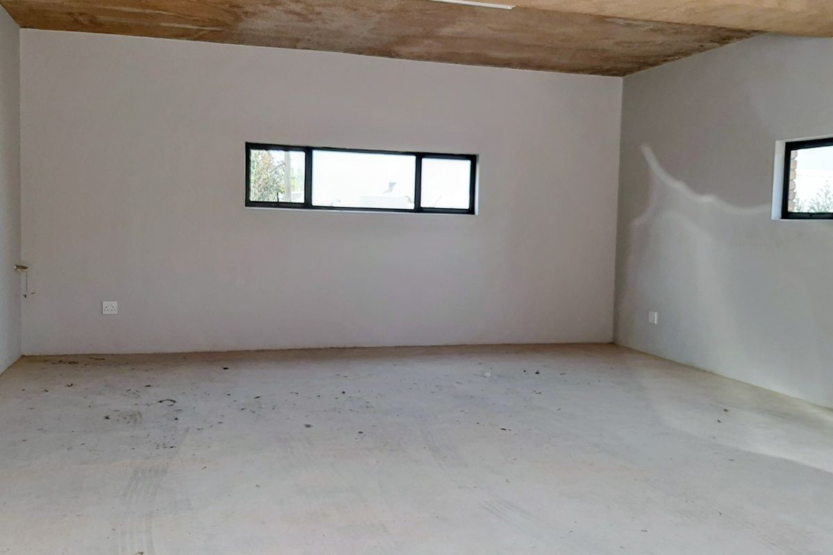 An unfinished interior space featuring exposed concrete ceilings, plastered walls, and aluminium window frames, ready for final flooring and decorative finishes.