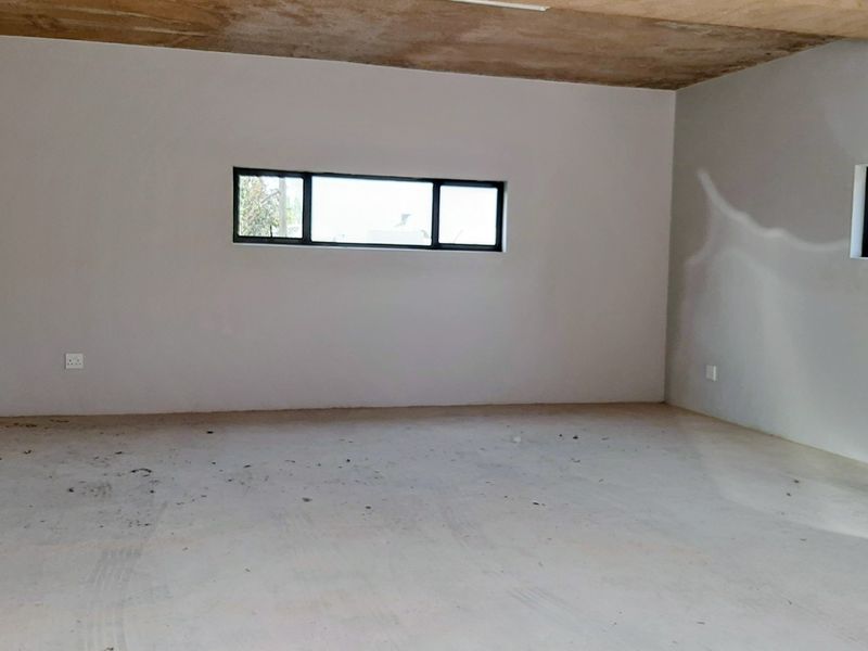 An unfinished interior space featuring exposed concrete ceilings, plastered walls, and aluminium window frames, ready for final flooring and decorative finishes.