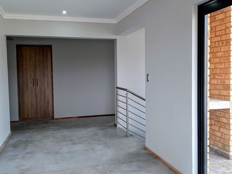 An open-plan landing area featuring a built-in cupboard, stainless steel balustrade, and direct access to an outdoor brick-built patio area.