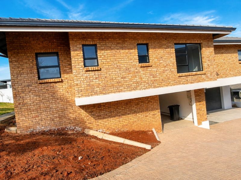 A modern face brick house exterior featuring a paved driveway, integrated garage, and aluminium window frames, set against a clear blue sky.