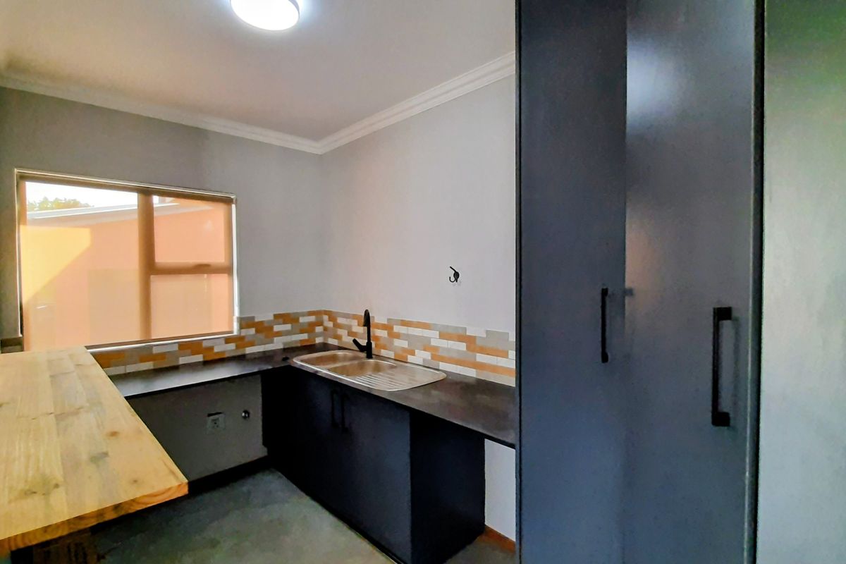 A clean, modern kitchen featuring dark cabinetry, contrasting timber and dark countertops, a stainless steel sink, and a decorative tiled splashback.