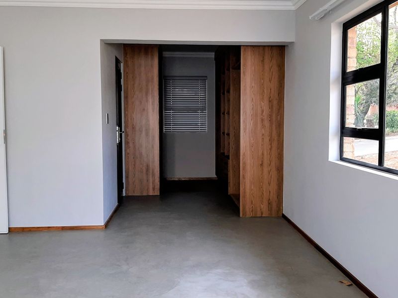 Spacious bedroom featuring polished concrete floors, built-in wooden cupboards, and large windows with venetian blinds, offering a clean and modern aesthetic.