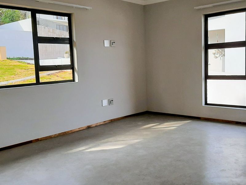 A bright, empty living area featuring polished concrete floors, large aluminium-framed windows, and neutral walls, ready for personalization.