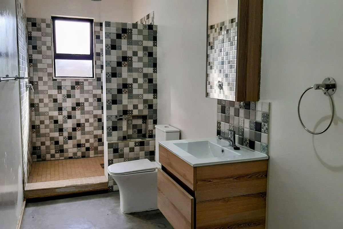 A modern bathroom featuring a walk-in shower with decorative mosaic tiling, a contemporary vanity unit with basin, and a wall-mounted medicine cabinet.
