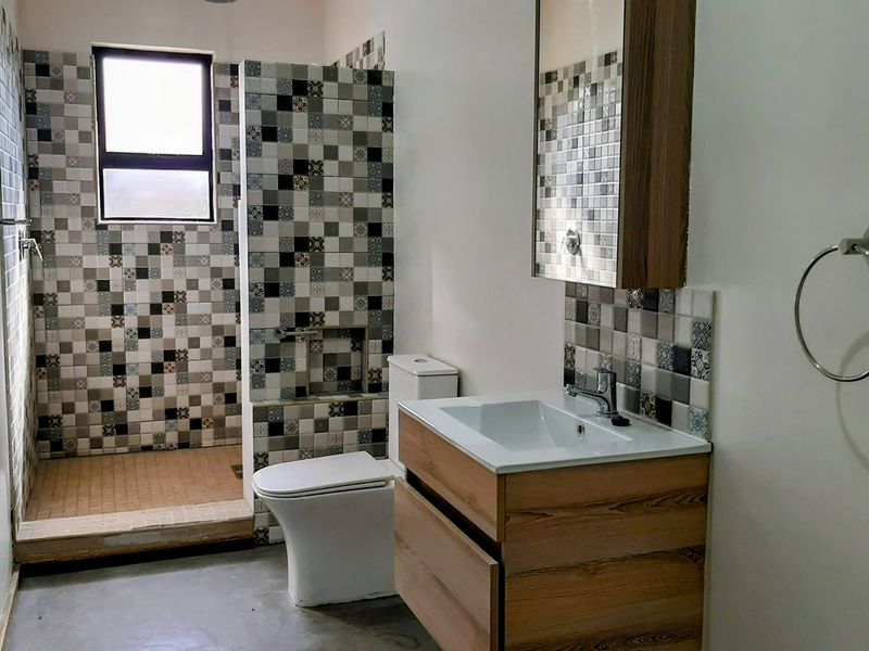 A modern bathroom featuring a walk-in shower with decorative mosaic tiling, a contemporary vanity unit with basin, and a wall-mounted medicine cabinet.
