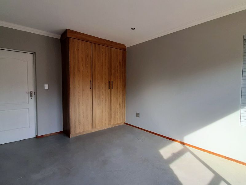 A clean, empty bedroom featuring neutral grey walls, built-in wooden cupboards, and fitted venetian blinds.