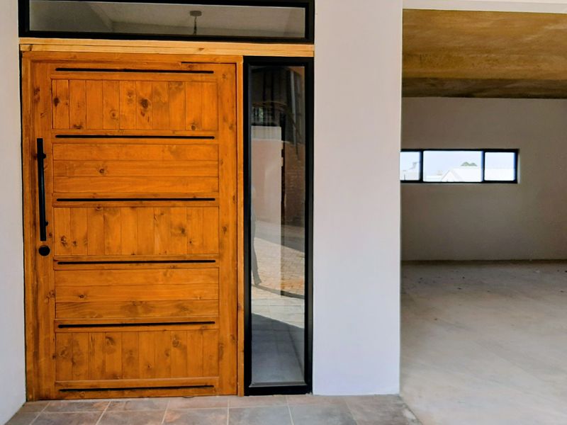 Entrance area featuring a modern timber front door with sidelight and transom windows, leading into an unfinished interior space with exposed concrete ceilings.