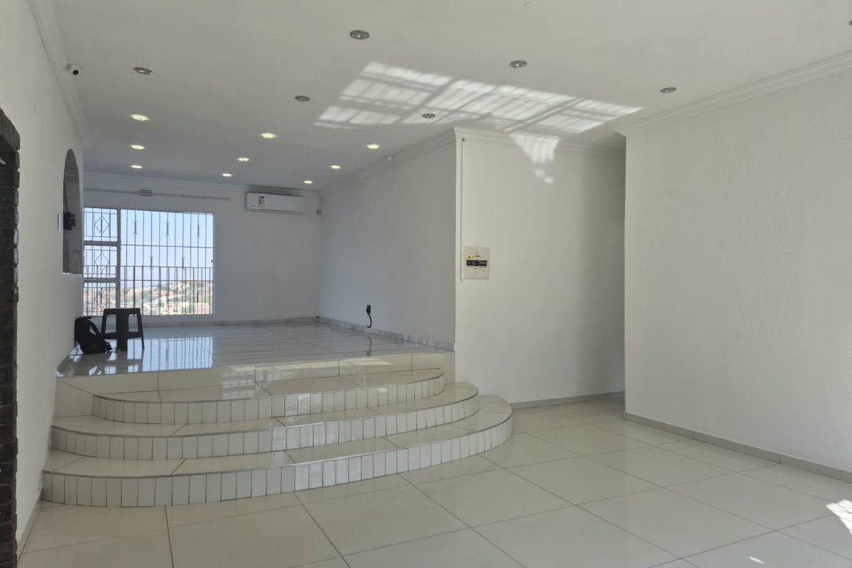 Spacious open-plan living area featuring a raised tiled platform, recessed downlighting, and a split-system air conditioner, offering a bright and versatile living space.