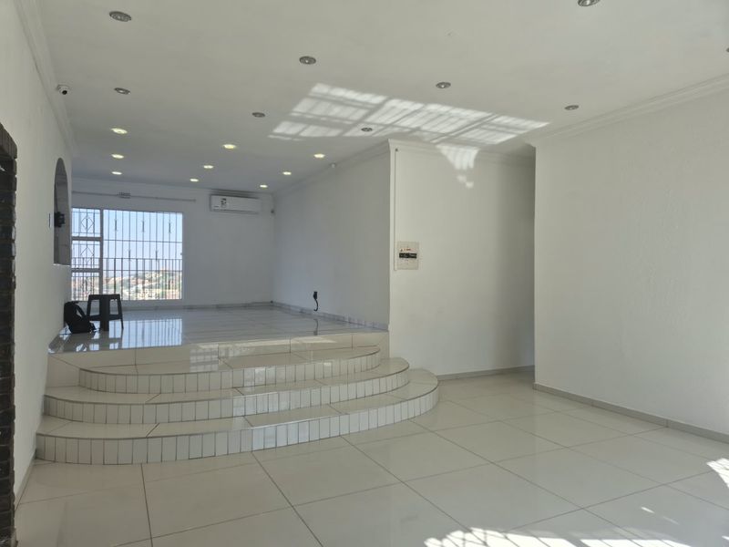 Spacious open-plan living area featuring a raised tiled platform, recessed downlighting, and a split-system air conditioner, offering a bright and versatile living space.
