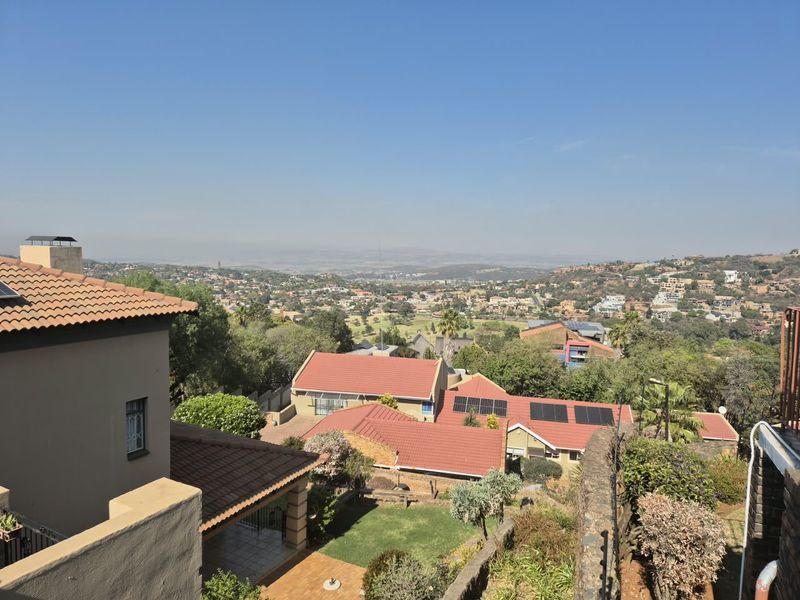 Elevated panoramic view overlooking a residential neighborhood with visible tiled roofs, solar installations, and landscaped garden areas.
