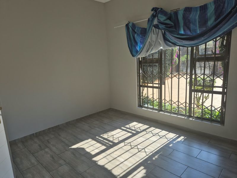 A bright, empty bedroom featuring modern wood-look floor tiles and secure window bars, offering a clean and neutral space ready for personalization.