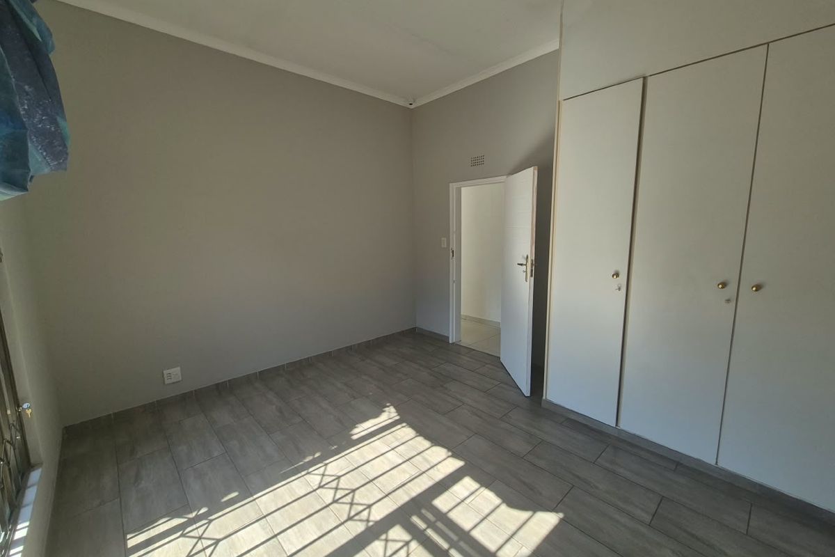 A clean, empty bedroom featuring modern wood-look tiled flooring and built-in cupboards, offering a neutral canvas for personalization.