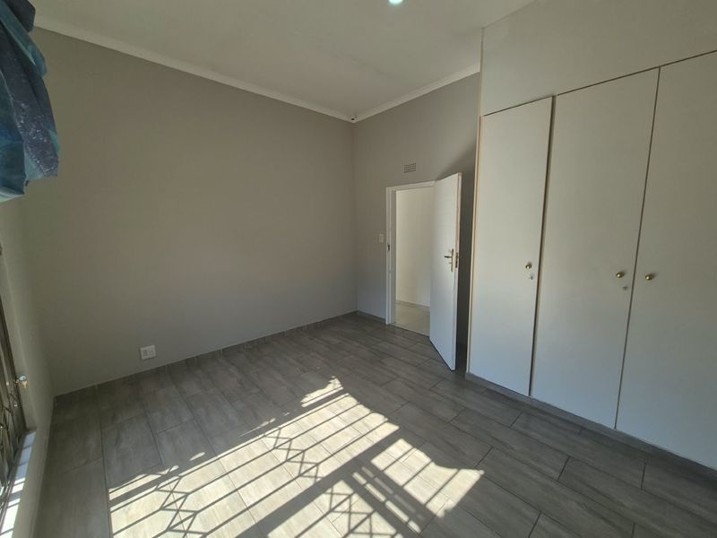 A clean, empty bedroom featuring modern wood-look tiled flooring and built-in cupboards, offering a neutral canvas for personalization.