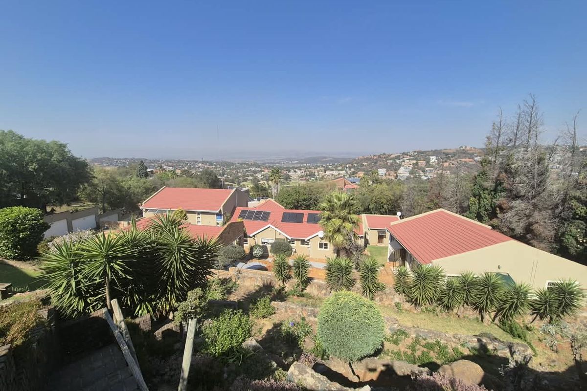 An elevated aerial view of the property featuring multiple buildings with metal roofing, solar panels, and a terraced garden overlooking the surrounding landscape.