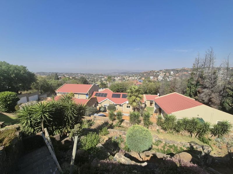 An elevated aerial view of the property featuring multiple buildings with metal roofing, solar panels, and a terraced garden overlooking the surrounding landscape.