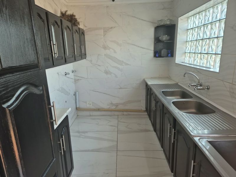 A functional scullery featuring dark cabinetry, double stainless steel sink, marble-look tiling, and a glass block window for natural light.