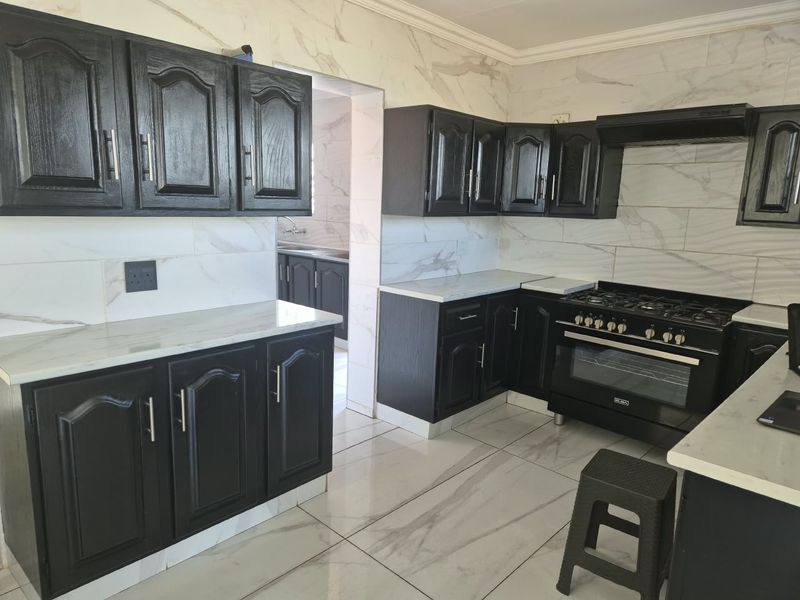 Modern kitchen featuring dark cabinetry, marble-look countertops, tiled flooring, and a built-in gas stove with an extractor fan.