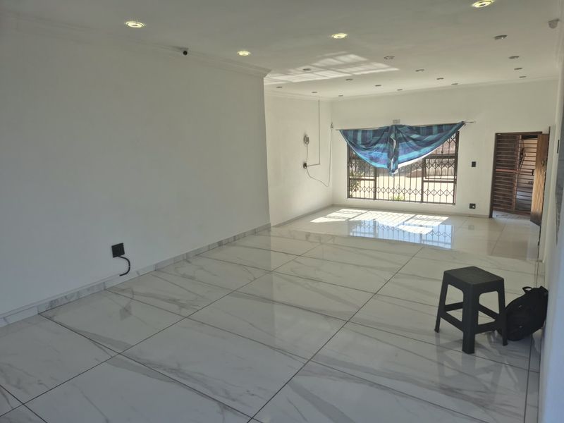 A bright, spacious, and empty living area featuring modern large-format porcelain floor tiles, recessed downlighting, and secure window and door access.