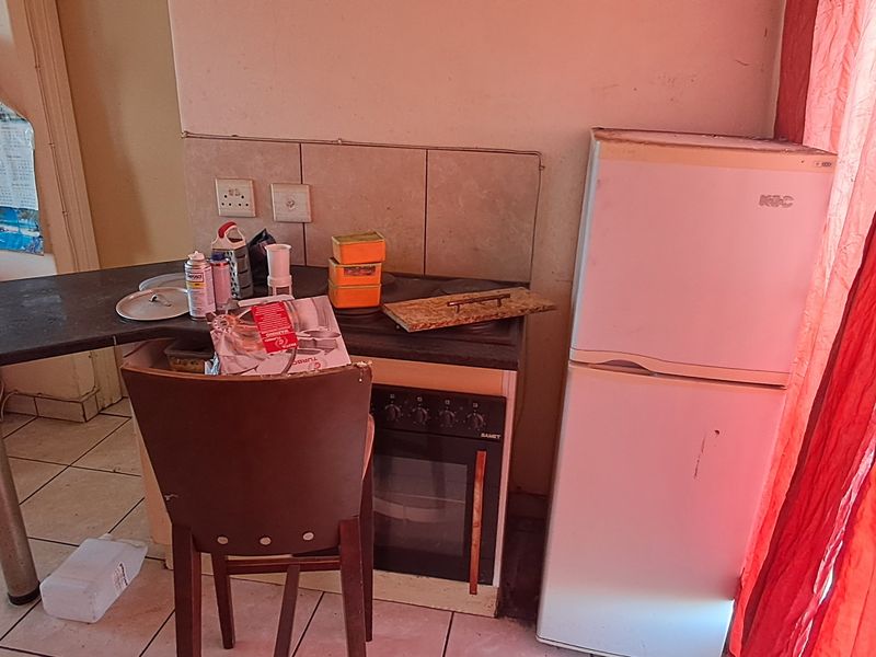 A compact kitchen area featuring a built-in oven, hob, tiled backsplash, and tiled flooring, currently showing signs of wear and dated finishes.