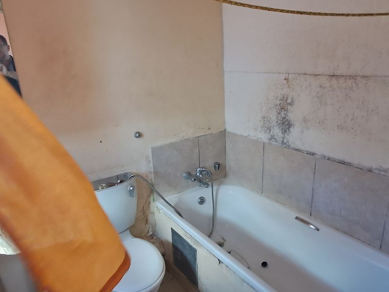 A dated bathroom featuring a bathtub, toilet, and pedestal basin, currently requiring significant renovation and wall surface repairs.