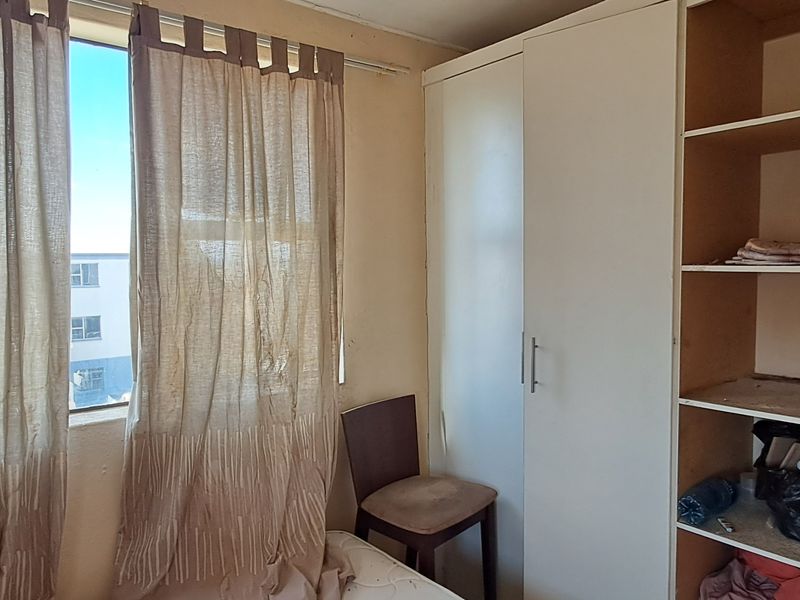 A bedroom featuring built-in cupboards and open shelving, offering functional storage space with potential for cosmetic updates.