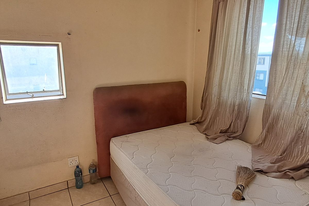 A bedroom featuring tiled flooring and natural light from dual windows, requiring cosmetic updates to the wall finishes.