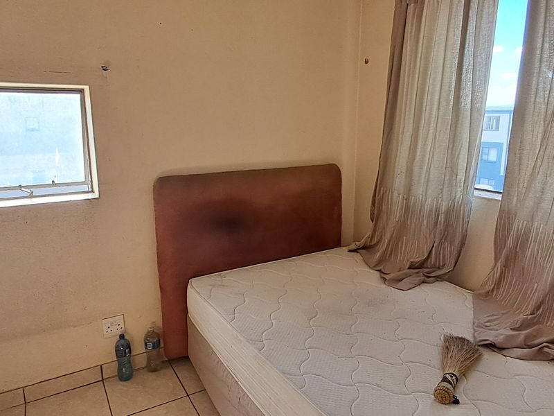 A bedroom featuring tiled flooring and natural light from dual windows, requiring cosmetic updates to the wall finishes.