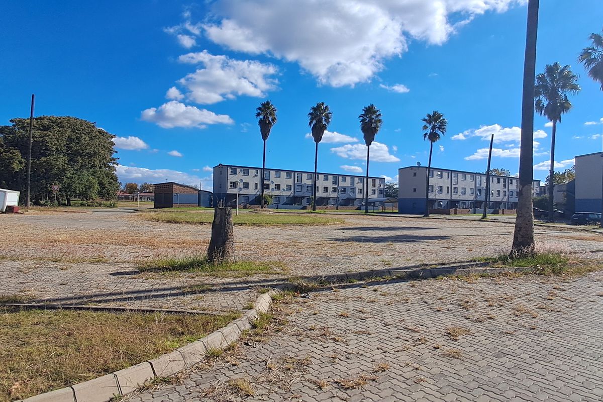 Exterior view of a multi-story apartment complex with a large paved parking area and mature palm trees.
