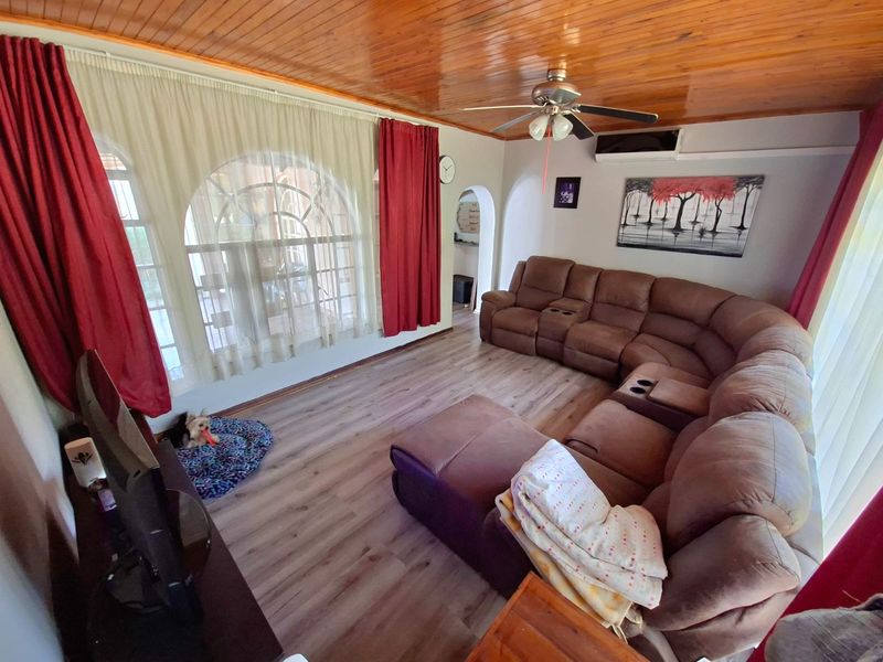 A comfortable living room featuring a warm timber-paneled ceiling, laminate flooring, and an arched window that allows for natural light.