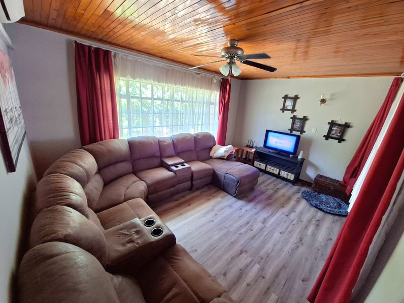 A comfortable living room featuring a warm timber-paneled ceiling, ceiling fan, and modern laminate flooring with a large window providing natural light.