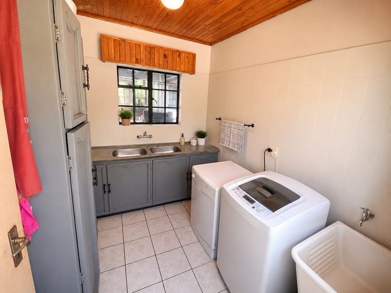 A functional laundry room featuring tiled walls and flooring, built-in cabinetry with a double sink, and a timber-paneled ceiling.