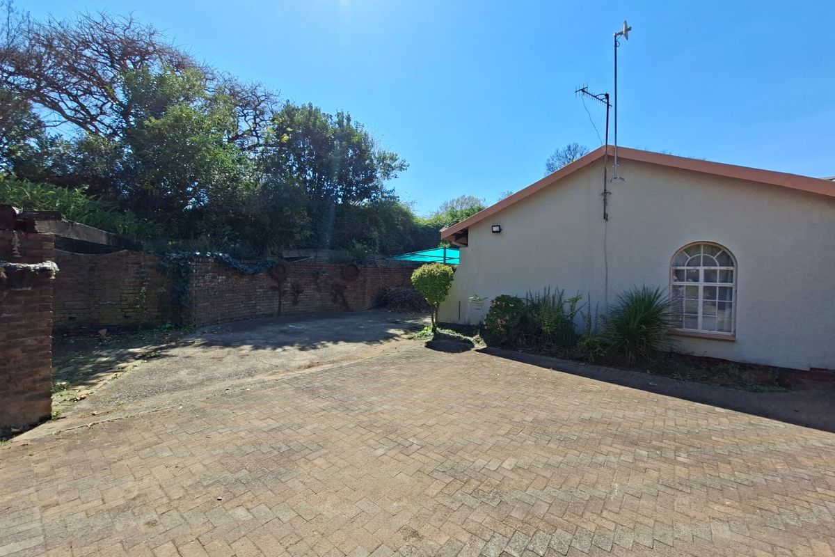 Rear exterior view featuring a paved courtyard area, brick boundary wall, and a side elevation of the house with an arched window.