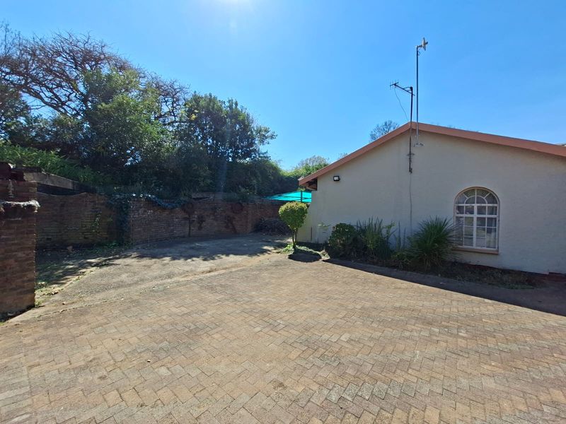 Rear exterior view featuring a paved courtyard area, brick boundary wall, and a side elevation of the house with an arched window.