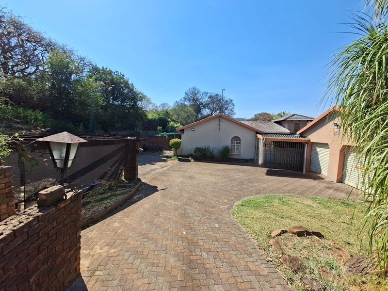 Front view of the property featuring a paved driveway, double garage, and brick boundary wall under a clear blue sky.