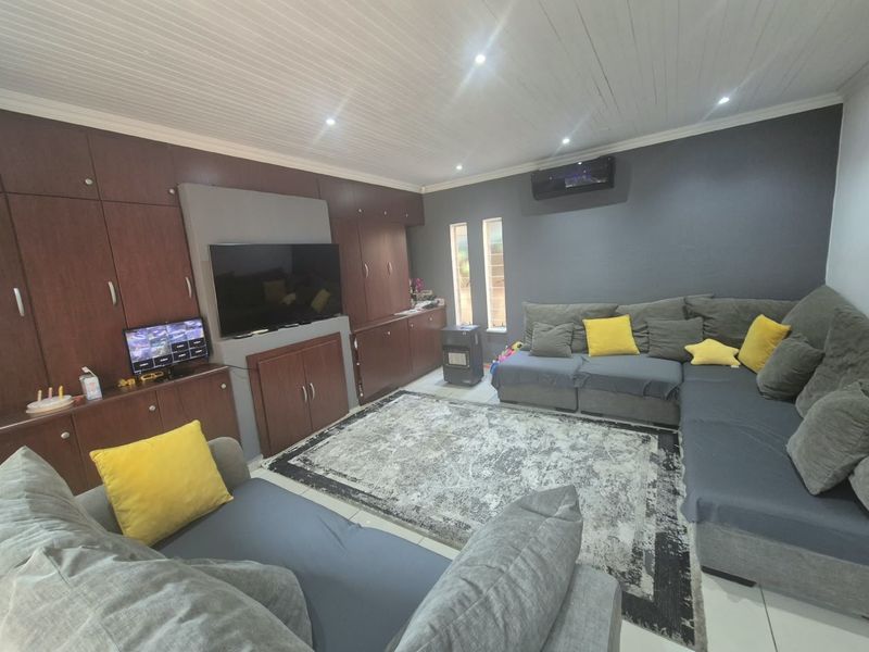 A comfortable living room featuring extensive built-in cabinetry, tiled flooring, recessed lighting, and a wall-mounted air conditioning unit.