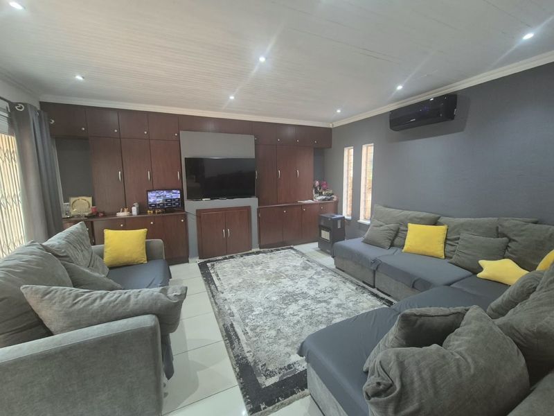 A comfortable living room featuring extensive built-in dark wood cabinetry, tiled flooring, recessed lighting, and a wall-mounted air conditioning unit.