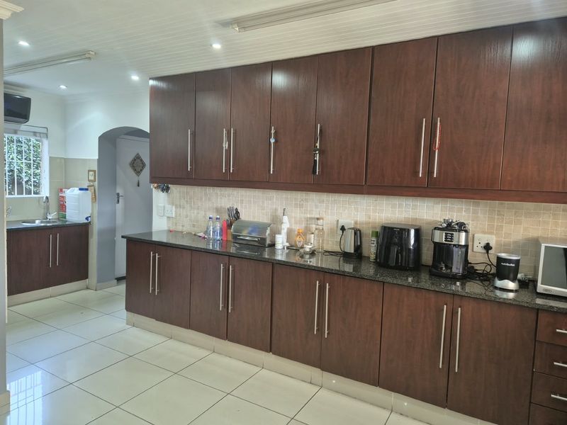 A functional kitchen featuring dark wood-finish cabinetry, granite countertops, a tiled backsplash, and light-colored ceramic floor tiles.