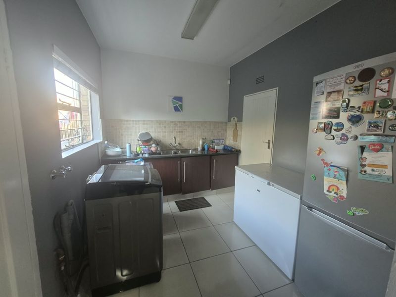 Functional laundry room featuring built-in cabinetry, a stainless steel sink, tiled backsplash, and tiled flooring with natural light from the side window.