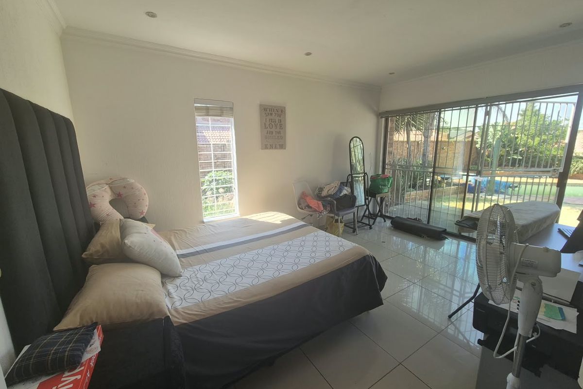 Spacious bedroom featuring tiled flooring, recessed lighting, and a large sliding glass door with security gate providing access to the outdoor area.