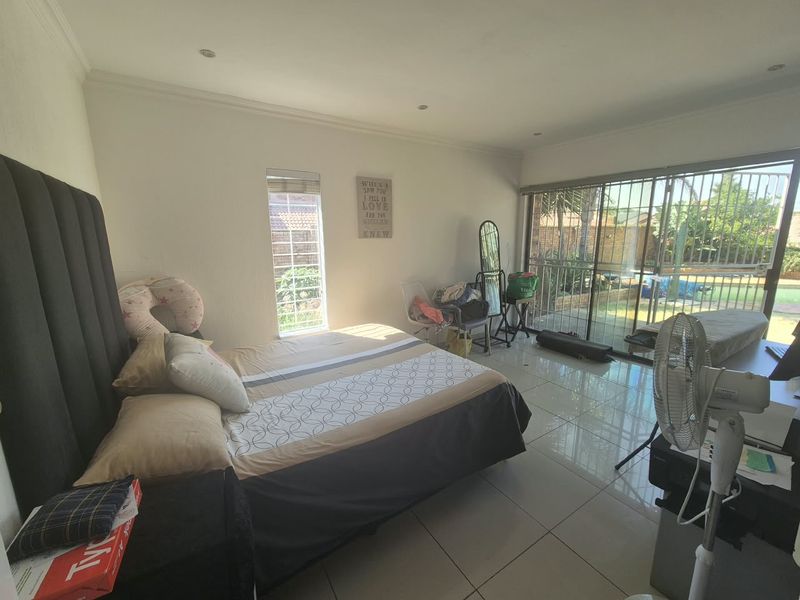 Spacious bedroom featuring tiled flooring, recessed lighting, and a large sliding glass door with security gate providing access to the outdoor area.