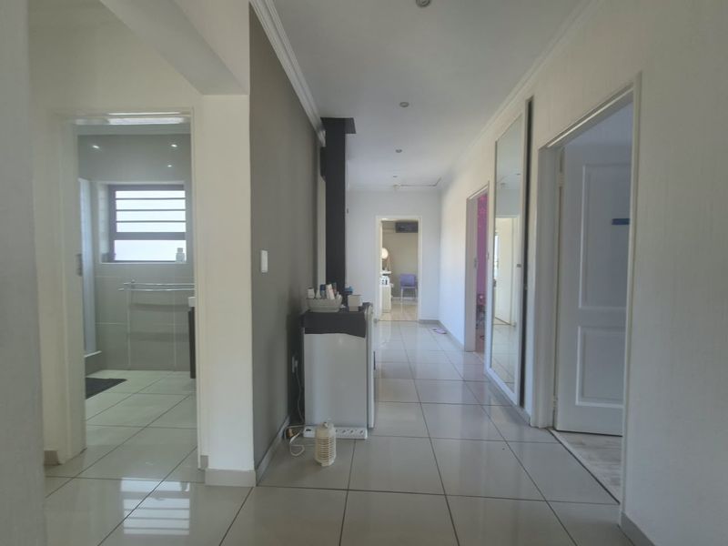A bright, tiled hallway featuring recessed lighting, coving, and a built-in fireplace, providing access to multiple rooms within the home.