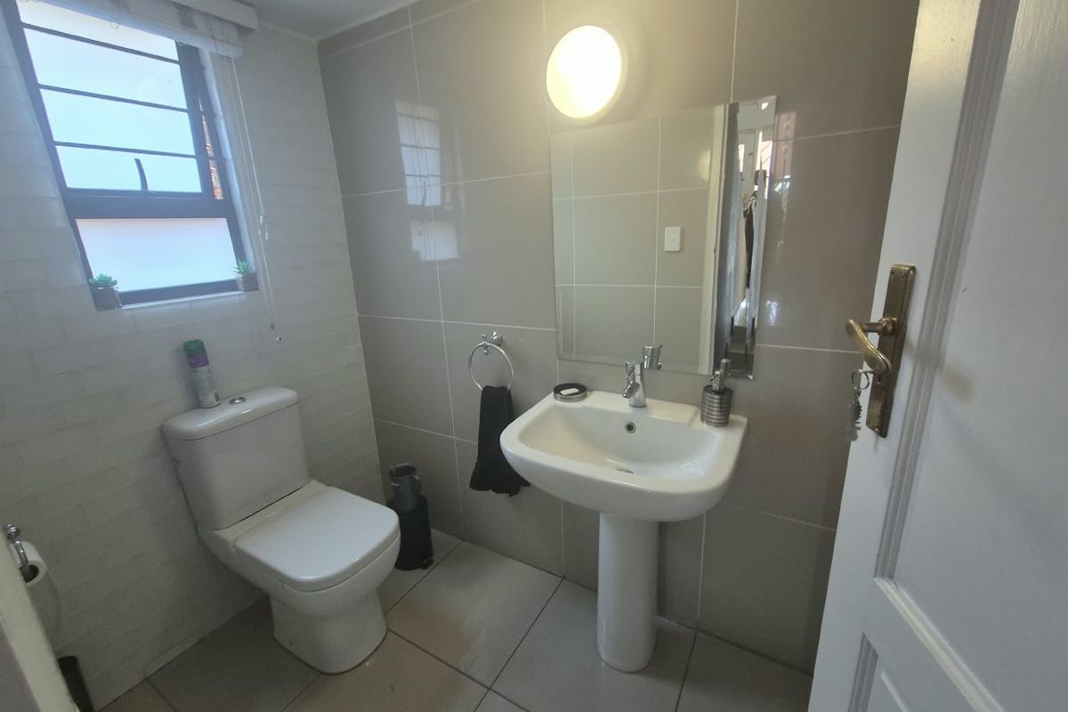 A clean and functional bathroom featuring a pedestal basin, toilet, and neutral wall tiling with a window for natural light.